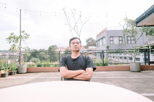 Thoughtful man sitting outdoors with crossed arms at urban rooft