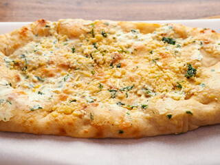 Flat sour dough bread with four cheeses on cooking paper and wooden table. Simple food. Italian style dish with high quality ingredients, Bakery product.