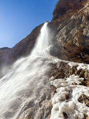 frozen winter waterfall with ice and snow on rocky cliffs under clear blue sky. dramatic nature scene with dynamic flow