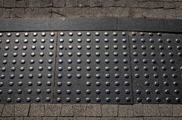 Tactile paving with raised dots designed to assist visually impaired pedestrians. Close-up of textured concrete surface in warm light. Accessibility infrastructure