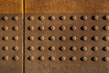 Tactile paving with raised dots designed to assist visually impaired pedestrians. Close-up of textured concrete surface in warm light. Accessibility infrastructure