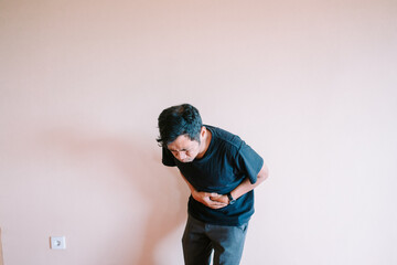 Man experiences acute stomach pain against plain wall backdrop
