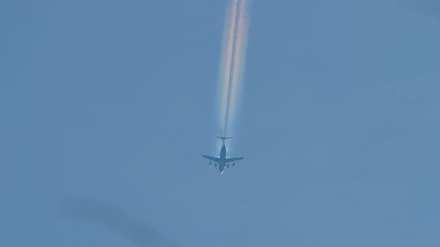Long shot of a passenger wide-body four-engine airliner flying with a beautiful rainbow contrail