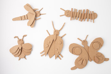 Fototapeta premium Handmade cardboard insect crafts arranged on white background. DIY eco-friendly bug figures including bee, butterfly, beetle, caterpillar, and moth. box craft for kids, toddler playtime,