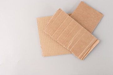 step in creative process, recycled paper materials for crafting, two pieces of cardboard placed on a grey surface. The top piece of cardboard is slightly smaller and has visible vertical ridges,