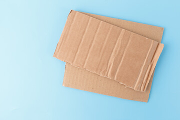 Two pieces of cardboard placed on blue surface. The top piece has vertical ridges and torn edge, bottom piece is smoother with horizontal lines. recycling, crafting, eco-friendly design