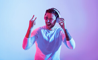 A young man dances joyfully, wearing headphones and illuminated by vibrant purple and pink...