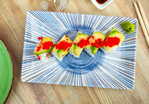 Uramaki sushi roll with salmon, mango, avocado, cucumber and tobiko served with soy sauce, wasabi and pickled ginger