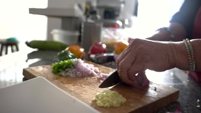 Elderly woman chopping red onions and garlic on wooden cutting board