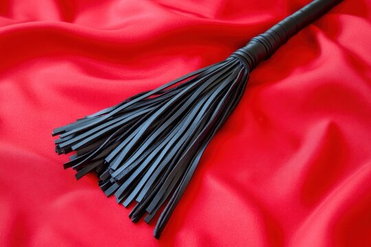 Leather flogger on luxurious red satin fabric, creating an elegant and dramatic scene.