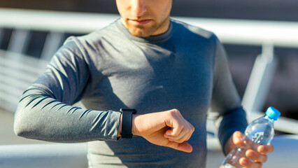 Time for training. Concentrated young man in wireless headphone with bottle of water looks at...