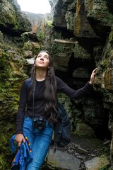 Adventurous young woman with a camera explores a moss-covered rocky canyon, looking up in awe. Natural landscape and outdoor travel photography