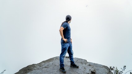 Smiling young man on a rocky cliff with a misty green valley in the background. Peaceful outdoor adventure in nature.