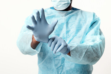 A man doctor, dressed in a surgical gown and gloves, focuses on putting on gloves in a clinical...