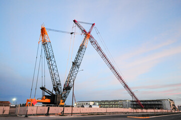 Large crawler cranes with lattice booms positioned at a data center construction site, supporting heavy lifting operations for structural assembly, with buildings under construction in the background