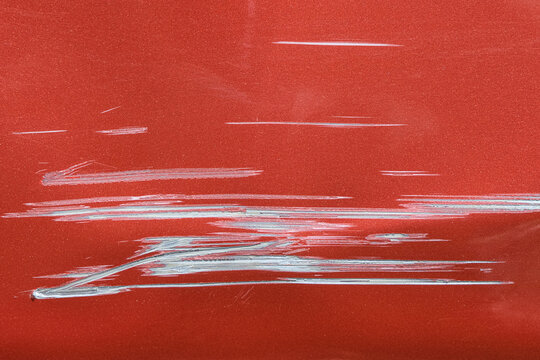 Close up of a red car with multiple visible scratches and paint damage The scratches expose the underlying metal, creating a contrast against the glossy surface. Perfect for automotive damage concepts