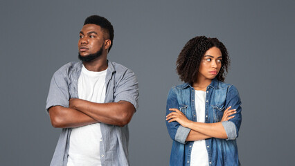 A young couple stands back to back, visibly upset, with crossed arms. Their expressions show tension as they confront their disagreement in a neutral setting, emphasizing their emotional disconnect.