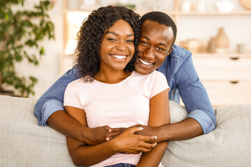 Obraz premium Beautiful black couple in love cuddling on sofa at home, free space