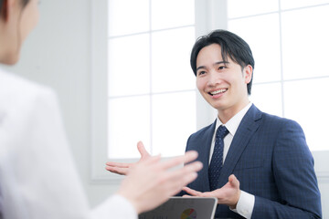 お客様に説明する若手の営業マンなどのイメージ