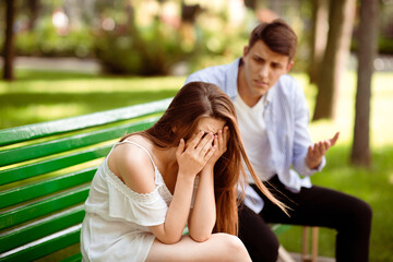 Fototapeta premium Depressed young girl crying during conflict with her boyfriend on bench at park