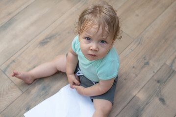 Naklejka premium Baby sitting on the floor holding a crayon near a blank paper