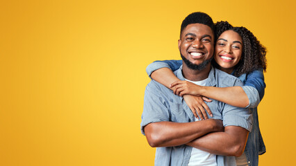Fototapeta premium A joyful couple embraces playfully, showcasing their happiness with warm smiles. The bright yellow background enhances their cheerful connection in a sunny atmosphere.