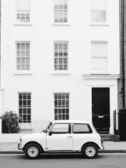 A white Mini Cooper parked gracefully in front of a classic London townhouse on a quiet street.