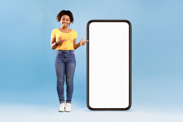 A young African American woman stands against a solid blue background, smiling confidently. She...