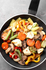 Different vegetables and mushrooms in frying pan on grey table, top view