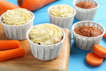 Tasty carrot muffins with fresh vegetables on light blue wooden table, closeup