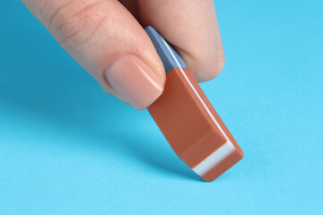 Woman using eraser on light blue background, closeup