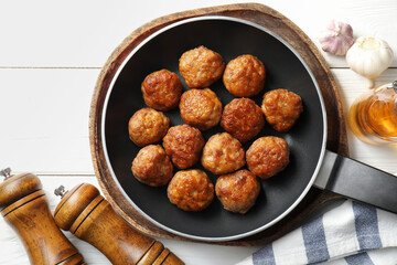 Tasty meatballs in frying pan and ingredients on white wooden table, flat lay