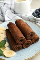 Delicious chocolate crepes with banana and blueberries served on light table, closeup