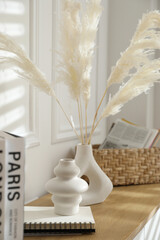 Vases with feathers and decor on wooden shelving unit indoors, closeup