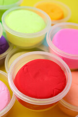 Different colorful modeling clay in plastic jars on yellow background, closeup
