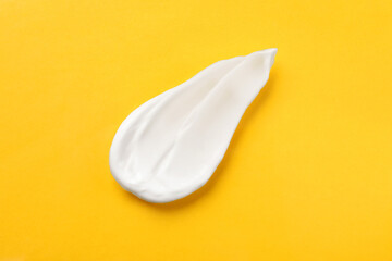 Smear of body cream on orange background, top view