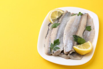 Marinated herring fillets with lemon and parsley on yellow background, closeup. Space for text