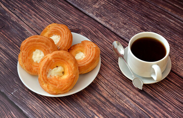 Plate with several custard tarts and a cup of black coffee on a wooden table.