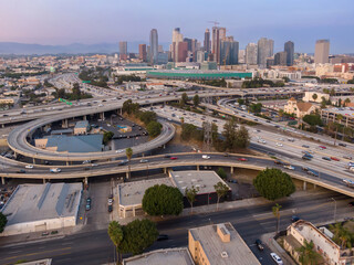 Naklejka na ściany i meble Aerial view of traffic flowing on the highway system in Los Angeles, California, USA. The photo shows the city skyline in the background.