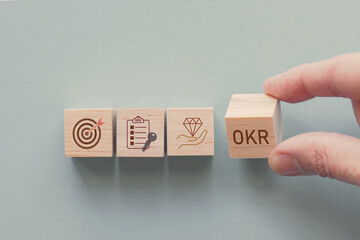 Hands holding wooden blocks with OKR icons, objective and key results concept
