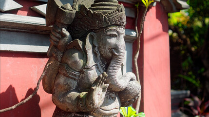 An old hindu stone statue of Ganesha covered with moss, standing on the street on the Bali