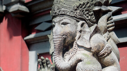 An old hindu stone statue of Ganesha covered with moss, standing on the street on the Bali