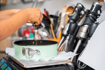 Pastry chef sprinkling crumbs into cake pan in professional kitchen