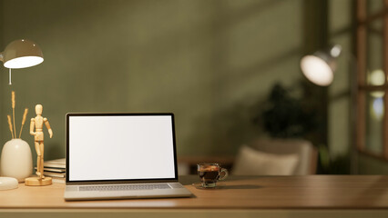 The white screen laptop and coffee cup place on wooden table with decor in the dim light green room.