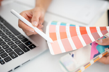 The hand holding a stylus pencil is choosing color from the printed color charts or color palettes.