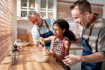 Caucasian senior gay couple baking bakery with adopted daughter in house. 