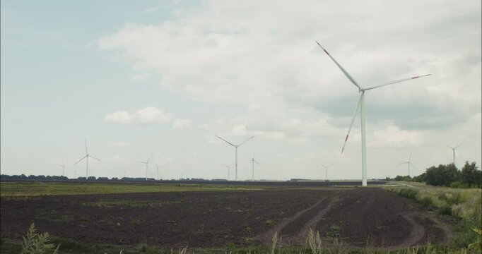 Wind turbines rotating in cultivated field under cloudy sky