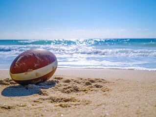 A rugby ball resting on golden beach sand, with the ocean waves and clear blue sky creating a serene coastal atmosphere.