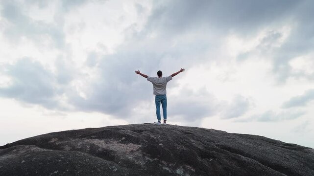 Man stands on giant rock arms outstretched for freedom, freedom signifying triumph over challenges, freedom embodying personal empowerment, perfect for adventurous marketing worldwide.