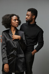 Elegant couple in black attire sharing a meaningful gaze against a neutral background, showcasing...